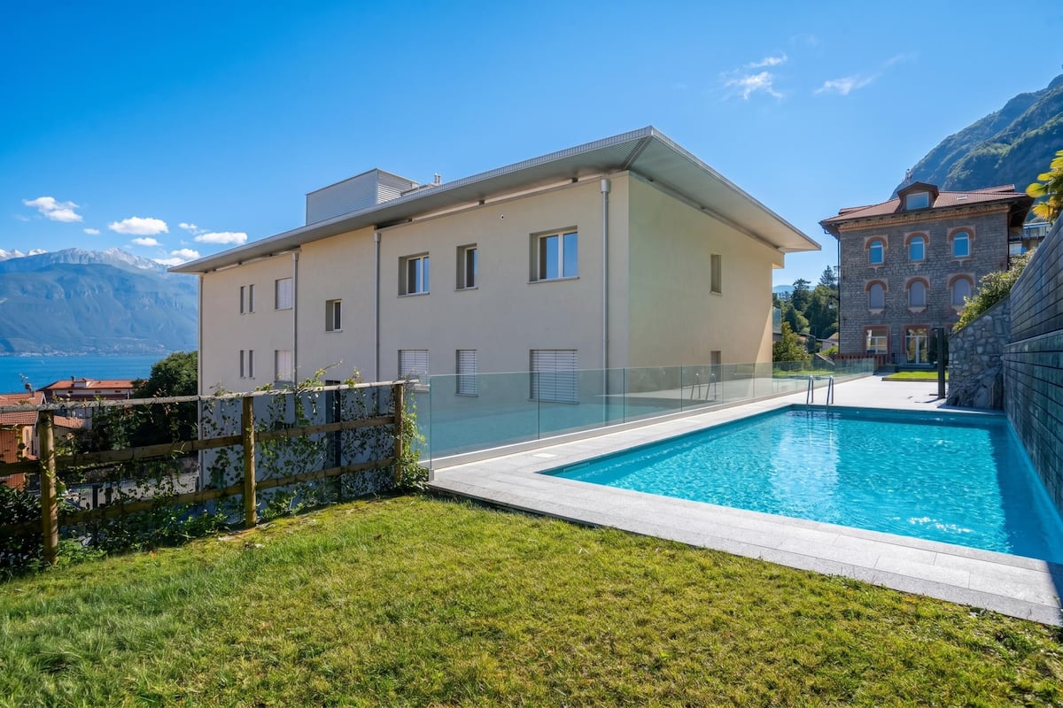 A modern building with a swimming pool, a clear view of the mountains, and a well-maintained lawn.