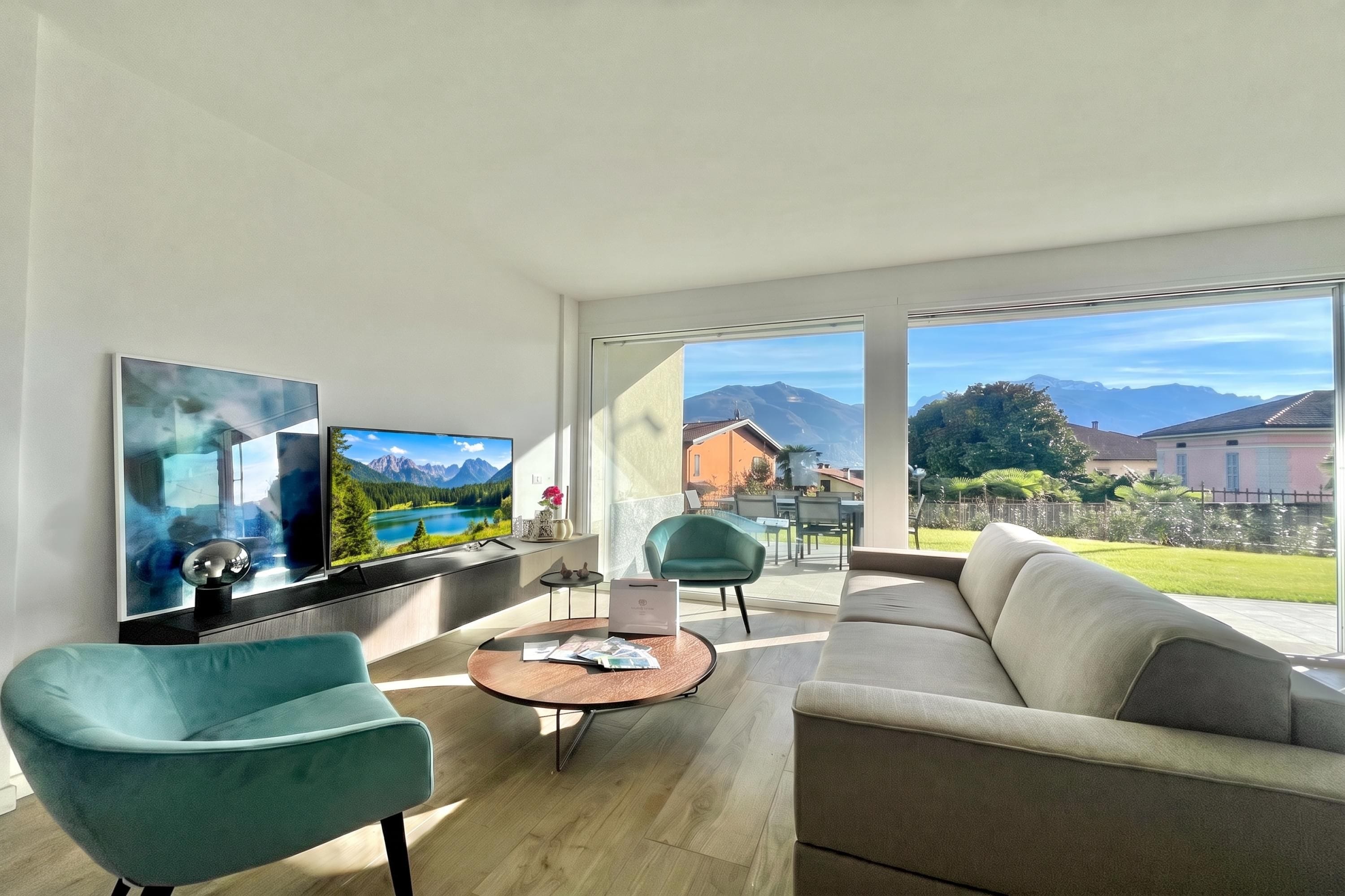 A modern living room with a sofa, two armchairs, a coffee table, and a TV displaying a mountain landscape.