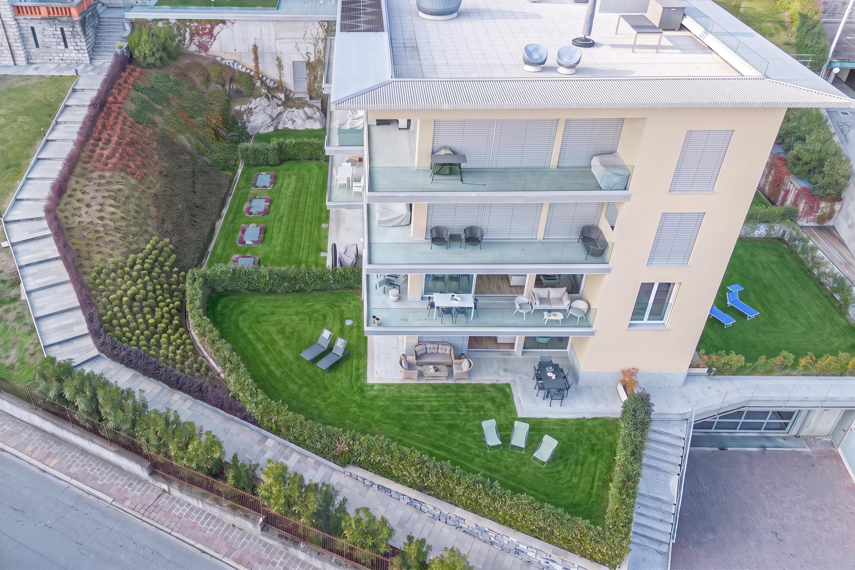 A modern multi-story building with a flat roof, outdoor seating area, and a well-maintained lawn.