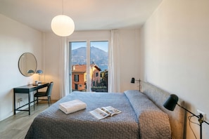 Una camera d'albergo moderna con un letto grande, una scrivania, una sedia e vista su una montagna e una città.