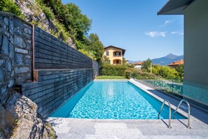 A swimming pool with a stone wall and a view of a mountain. - Modern House Apartments (Menaggio)
