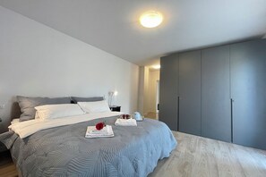 A modern bedroom with a large bed, grey bedding, a bedside table with a lamp, and a wardrobe. - Modern House Apartments (Menaggio)