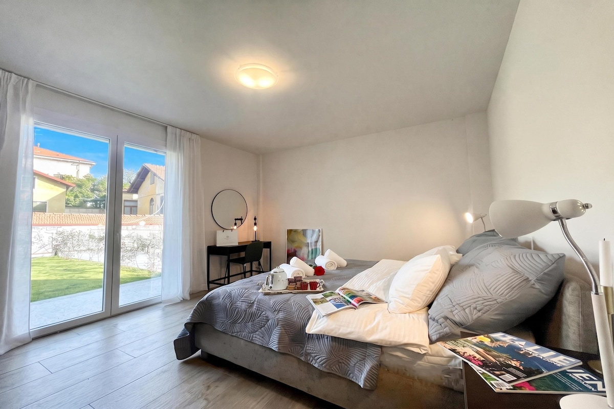 A bedroom with a bed, a desk, a chair, a window, and a view of the outside.