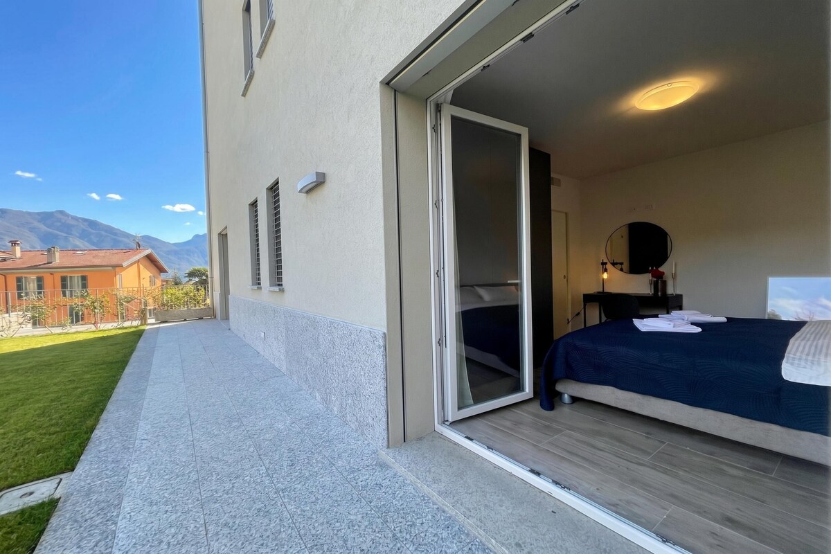A hotel room with a bed, a small desk, a mirror, and a sliding glass door leading to a balcony.