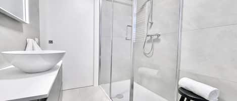 A modern bathroom with a glass shower enclosure, a white sink with a bowl, and a black stool with a towel.