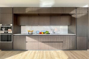 A modern kitchen with built-in appliances, a marble backsplash, and a wooden floor. - Modern House Apartments (Menaggio)