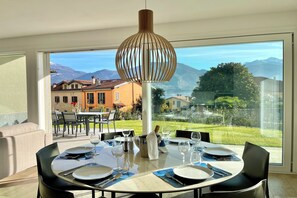 Uma área de refeições com uma mesa posta para quatro pessoas, uma luminária pendente e vista para uma paisagem montanhosa através de amplas janelas.
