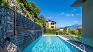 A swimming pool with a stone wall and a view of a mountain. - Modern House Apartments (Menaggio)
