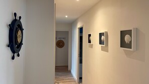 Enter a nautical-themed hallway leading to a cozy room with a door featuring a woven mat and framed ocean-inspired decor.