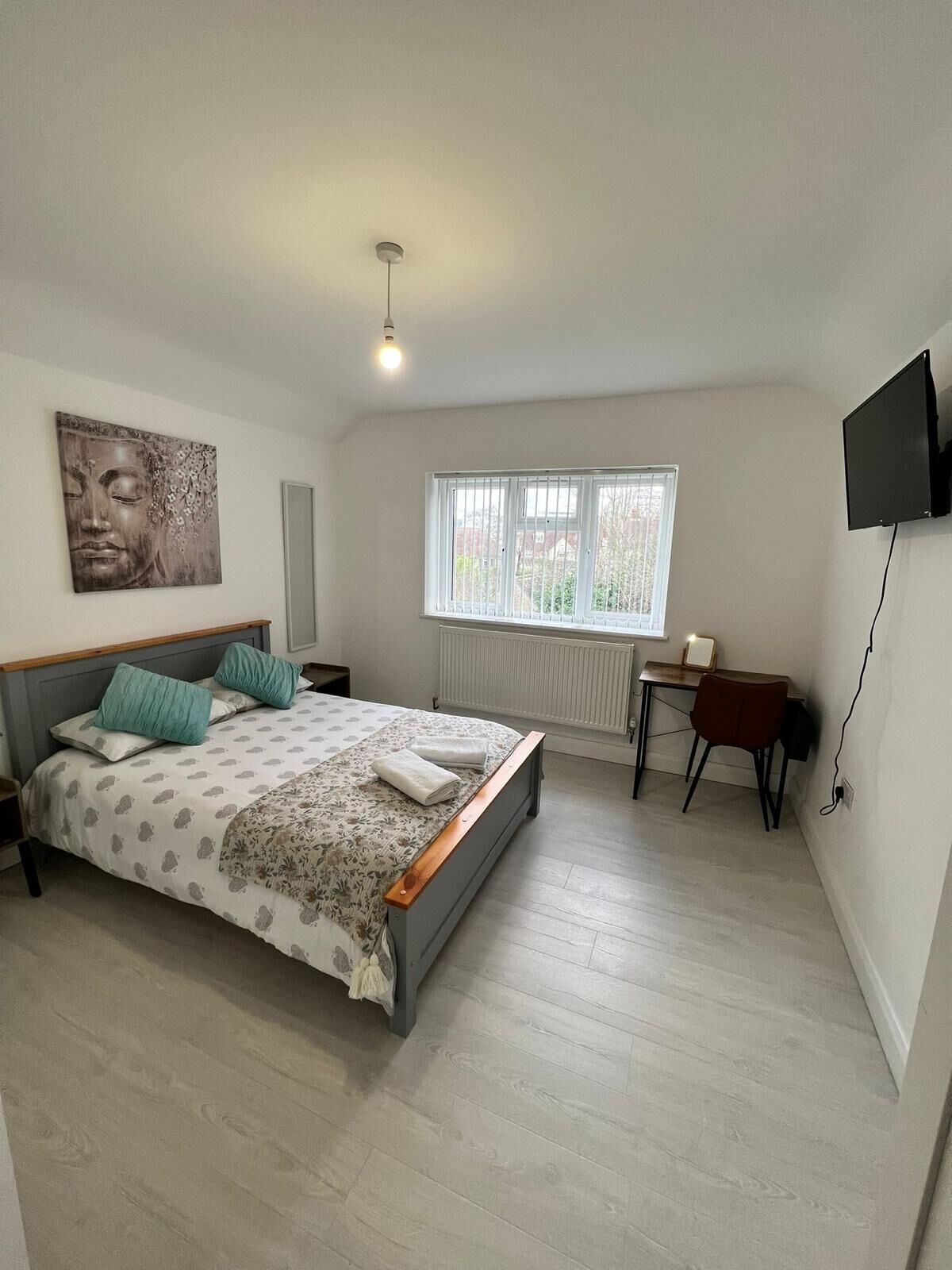 Un dormitorio con cama, escritorio, silla, televisor y ventana.