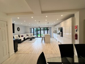 Eine moderne Küche mit weißen Schränken, einer zentralen Kücheninsel und einem Essbereich mit Glastisch und schwarzen Stühlen.