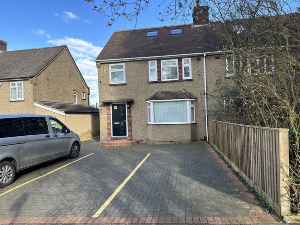 A residential area with a paved driveway leading to a house with a black door and a garage door. - Beautiful home in Oxford (Headington)