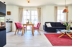Uma sala de estar moderna com um sofá preto, duas cadeiras vermelhas, uma mesa de jantar de madeira e um tapete vermelho.