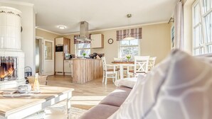 A modern living room with a fireplace, a dining area, and a kitchen with a central island. - Ferienhaus Haubenlerche 20 - Der Natur Ganz nah (Fuhlendorf)