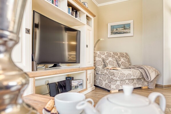 Una sala de estar con televisor de pantalla plana, estanterías, un sofá estampado y una mesa con tetera y tazas.
