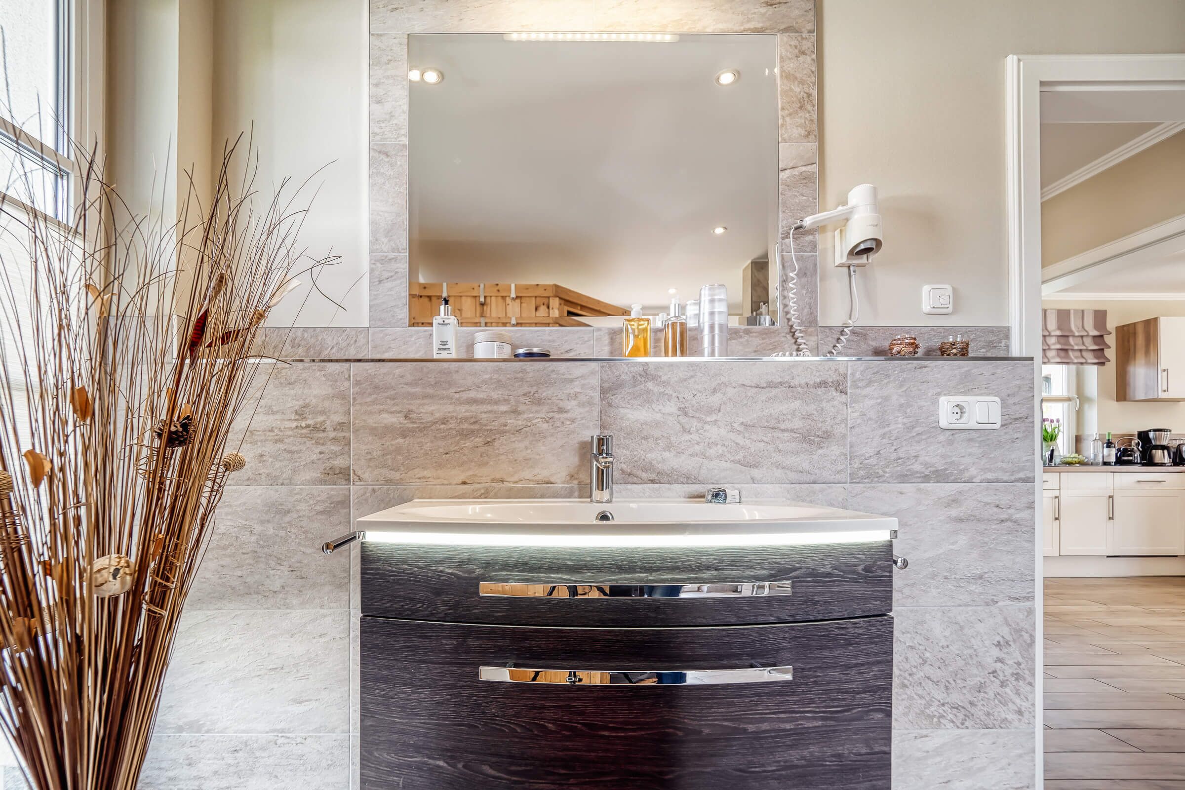 Une salle de bain moderne avec un lavabo en marbre, un grand miroir et un sèche-cheveux posé sur le comptoir.