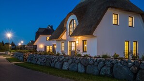 Una hilera de casas con tejados de paja y paredes blancas, rodeadas por un muro de piedra y un camino pavimentado.