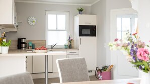 Una cocina moderna con armarios blancos, un microondas negro y una ventana. Hay un fregadero, una cafetera y un bol de fruta en la encimera.