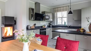 A modern kitchen with a built-in fireplace, wooden dining table, and red chairs. - Ferienhaus Seeadler 7 - Der Natur Ganz nah (Fuhlendorf)