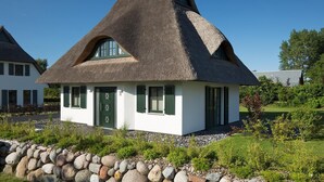 A traditional thatched-roof house with a green door and shutters, surrounded by a stone wall and greenery. - Ferienhaus Seeadler 7 - Der Natur Ganz nah (Fuhlendorf)