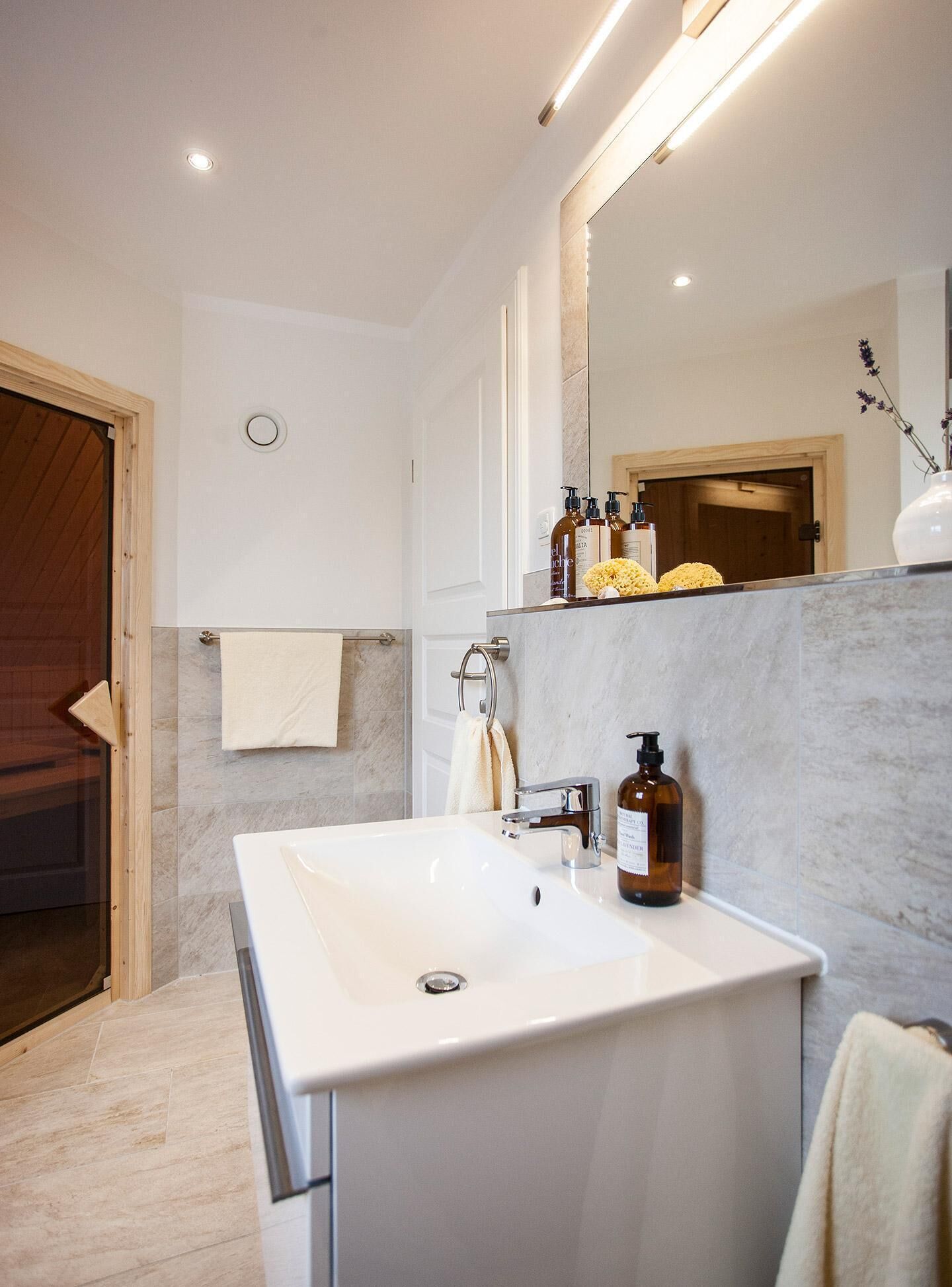 Un baño moderno con un lavamanos grande de color blanco, un espejo y una puerta de madera.