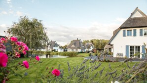 Un entorno de pueblo tranquilo con casas tradicionales, un estanque y abundante vegetación.