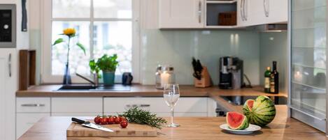 A modern kitchen with a wooden countertop, a cutting board with tomatoes, a glass of water, and a watermelon.