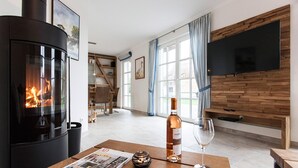Una sala de estar acogedora con una estufa de leña, una mesa de madera con una botella de vino y una copa, y un televisor montado en una pared de madera.