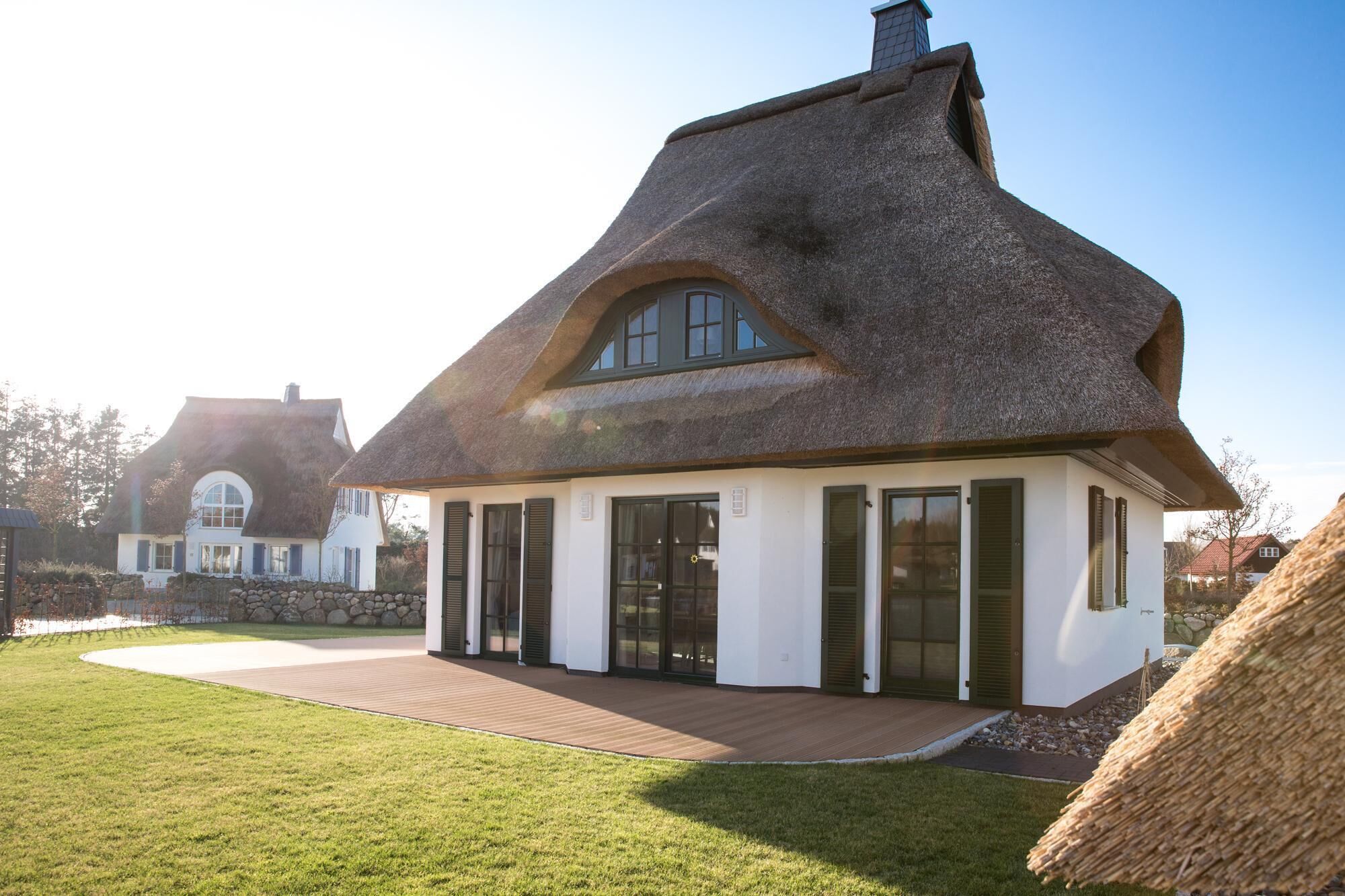 A house with a thatched roof, white exterior walls, and a wooden deck.