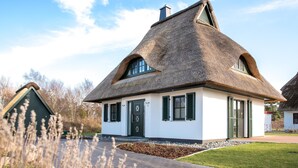 Ein traditionelles Haus mit Strohdach, weißen Wänden und grünen Fensterläden.