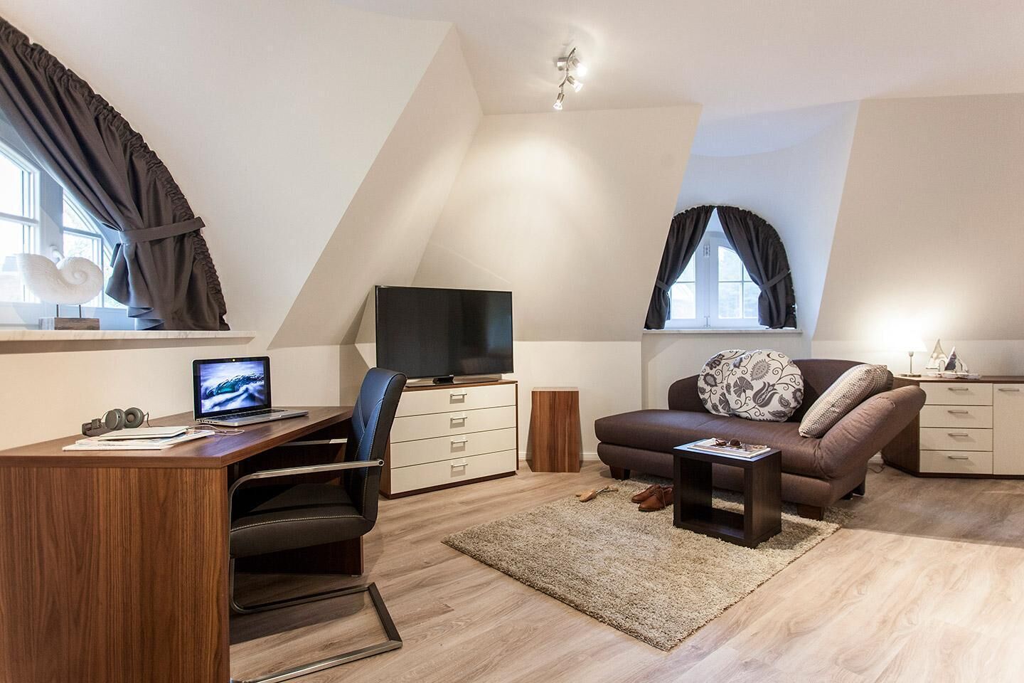 Un salon moderne doté d’un téléviseur à écran plat, d’un bureau avec un ordinateur portable, d’un canapé agrémenté de coussins décoratifs et d’une petite table d’appoint.
