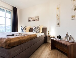 Moderni hotellihuone, jossa on suuri sänky, puinen työpöytä ja näkymä ulos.