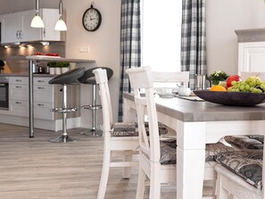 Une cuisine moderne avec des meubles blancs, un plan de travail en bois et un coin repas comprenant des chaises blanches et un banc.