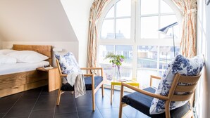 Un dormitorio con cama de madera, mesita de noche, silla, pequeña mesa y ventana con cortinas.