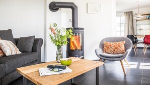 Una sala moderna con una chimenea de leña, un sillón gris y una mesa de centro de madera con un jarrón de flores.