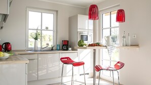 Una cucina moderna con pensili bianchi, una cappa in acciaio inossidabile, un bollitore rosso e una macchina per il caffè. Sono presenti due sgabelli da bar rossi e una finestra con vista sul verde.
