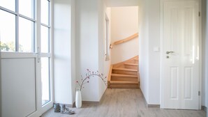 Un corridoio con una scala in legno, una porta bianca e una finestra che si affaccia sugli alberi.
