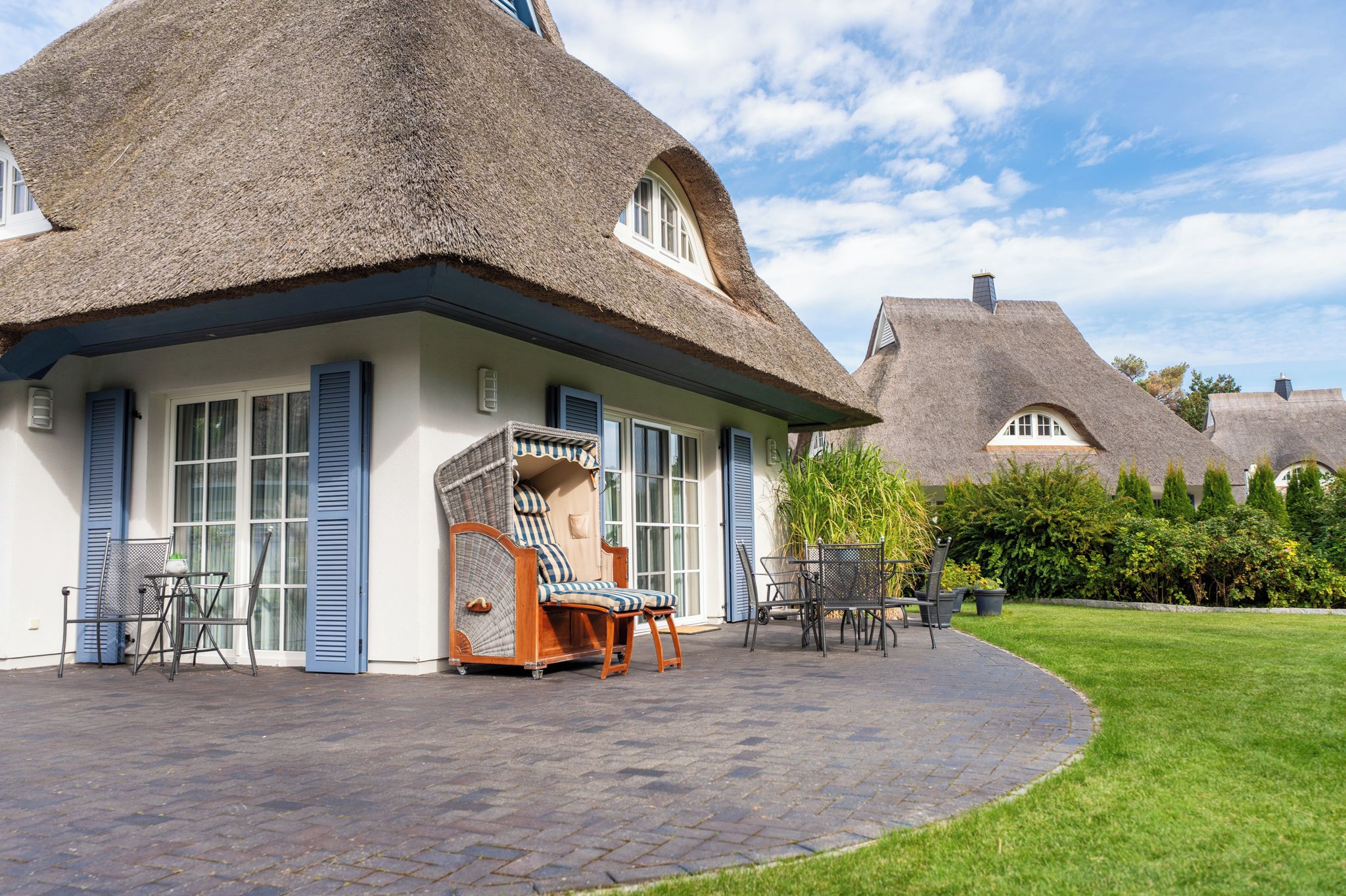 A thatched-roof house with a paved patio, outdoor seating, and a well-maintained lawn.