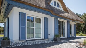 A modern house with a thatched roof, large windows with shutters, and a paved driveway. - Ferienhaus Haubenlerche 16 - Der Natur Ganz nah (Fuhlendorf)