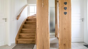 A wooden staircase with a handrail, white walls, and a door with heart-shaped decorations. - Ferienhaus Haubenlerche 16 - Der Natur Ganz nah (Fuhlendorf)