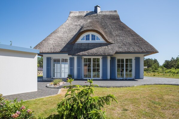 A house with a thatched roof, large windows, and a well-maintained lawn. - Ferienhaus Haubenlerche 16 - Der Natur Ganz nah (Fuhlendorf)