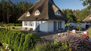 A traditional thatched-roof house with a white exterior, a front porch, and a well-maintained garden with various plants and flowers. - Ferienhaus Haubenlerche 16 - Der Natur Ganz nah (Fuhlendorf)