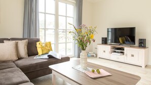 A living room with a sofa, coffee table, TV, and a vase of flowers. - Ferienhaus Seeschwalbe 10 - Der Natur Ganz nah (Fuhlendorf)