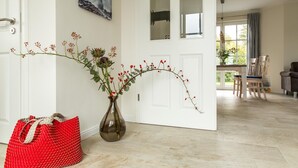 A hallway with a vase of red berries and artichokes, a red woven bag, and a painting of a bridge. - Ferienhaus Seeschwalbe 10 - Der Natur Ganz nah (Fuhlendorf)