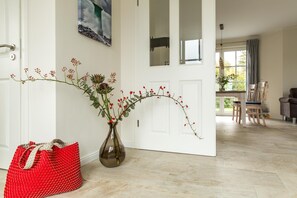 Un couloir orné d’un vase rempli de baies rouges et d’artichauts, d’un sac rouge tissé et d’un tableau représentant un pont.
