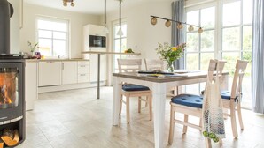 A modern kitchen with white cabinets, a built-in microwave, and a wood-burning stove. - Ferienhaus Seeschwalbe 10 - Der Natur Ganz nah (Fuhlendorf)