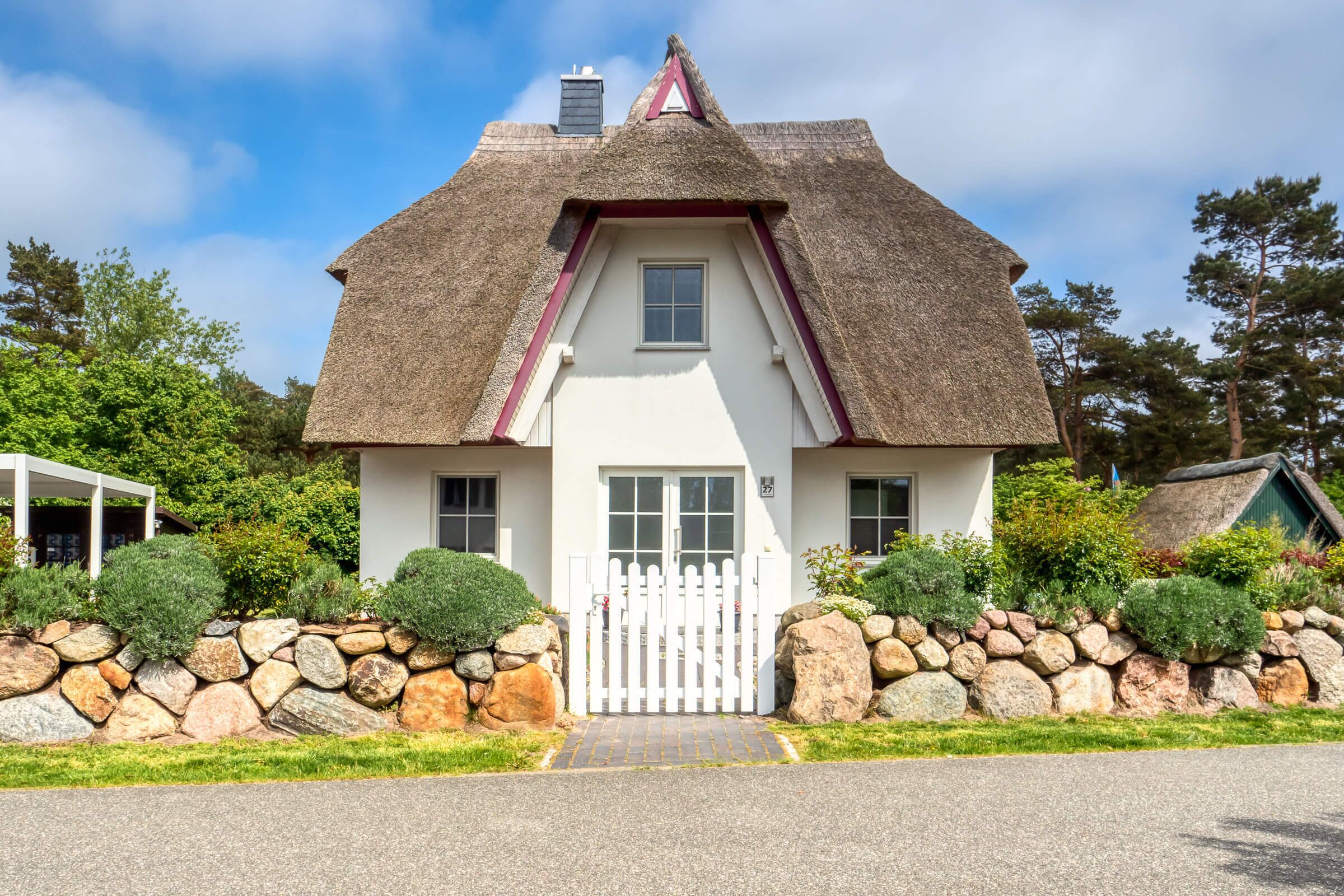 Une maison avec un toit de chaume, des murs blancs et un mur de pierre qui entoure la propriété.
