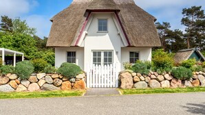 A house with a thatched roof, white walls, and a stone wall surrounding the property. - Ferienhaus Seeschwalbe 10 - Der Natur Ganz nah (Fuhlendorf)