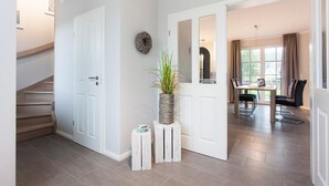 A modern hallway with a staircase, a potted plant, and a dining area with a table and chairs. - Ferienhaus Seeschwalbe 37 - Der Natur Ganz nah (Fuhlendorf)
