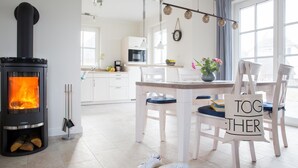 Eine moderne Küche mit Kaminofen, weißen Schränken und einem Essbereich mit Stühlen und Tisch.
